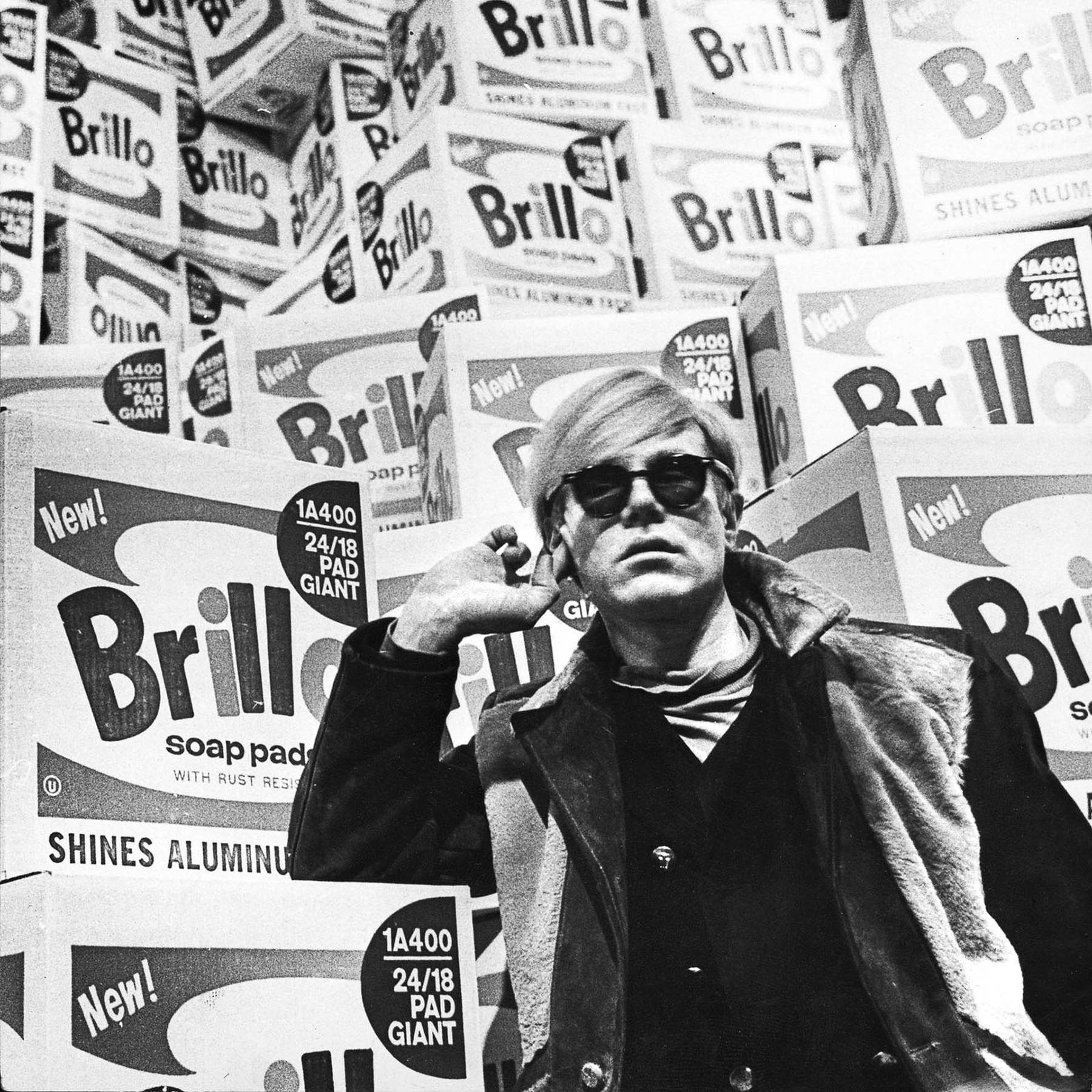 Picture of Andy Warhol in front of Brillo boxes.